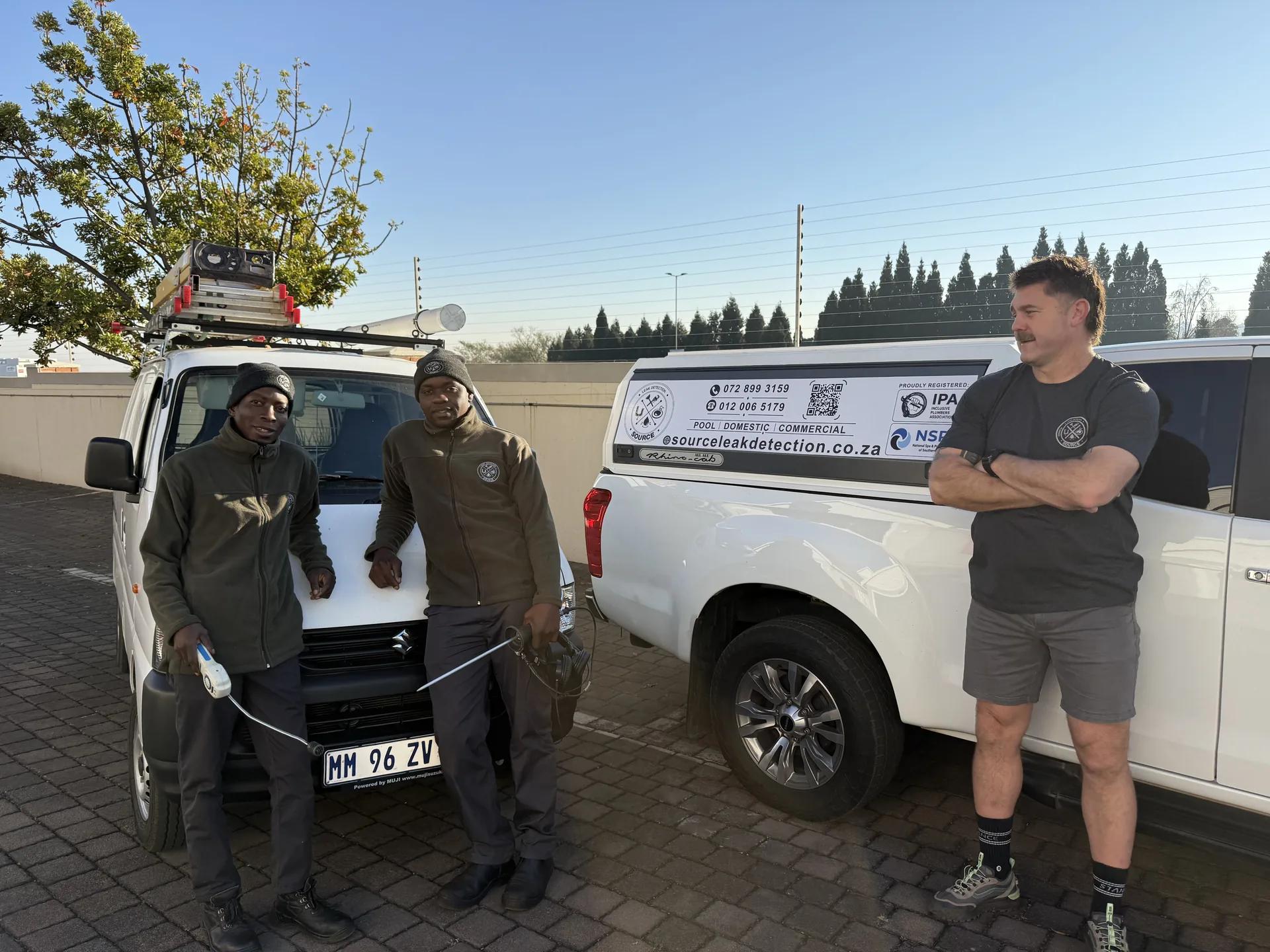 Source Leak Detection team of three next to a branded Suzuki bakkie with acoustic detection equipment on the roof rack — visible IPA and NSPI accreditation badges on the canopy